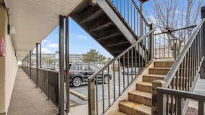 A covered outdoor area with a staircase leading to an upper level, adjacent to a sidewalk and street. - BayCation Walk to Jolly Roger + Beach (Ocean City)