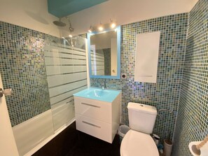 Ein Badezimmer mit Duschkabine aus Glas, einem weißen Waschbecken mit blauer Arbeitsplatte und einer weißen Toilette.