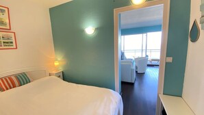 Ett hotellrum med en säng, ett nattduksbord, en lampa och utsikt över en balkong med en stol.