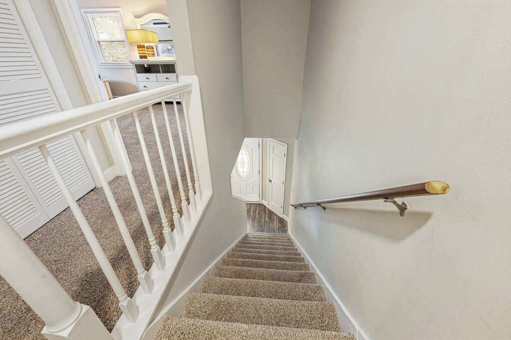 Eine Treppe mit weißer Brüstung und Teppichstufen führt zu einer Empore mit einer weißen Tür und einer Lampe.