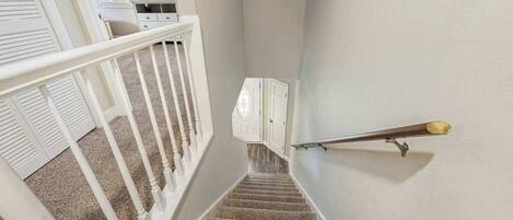 Eine Treppe mit weißer Brüstung und Teppichstufen führt zu einer Empore mit einer weißen Tür und einer Lampe.