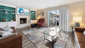 A modern living room with a fireplace, leather sofas, a glass coffee table, and a sign for Big Fish Rentals. - Spacious Home 3BR Close to Beach Centrally Located (Myrtle Beach)