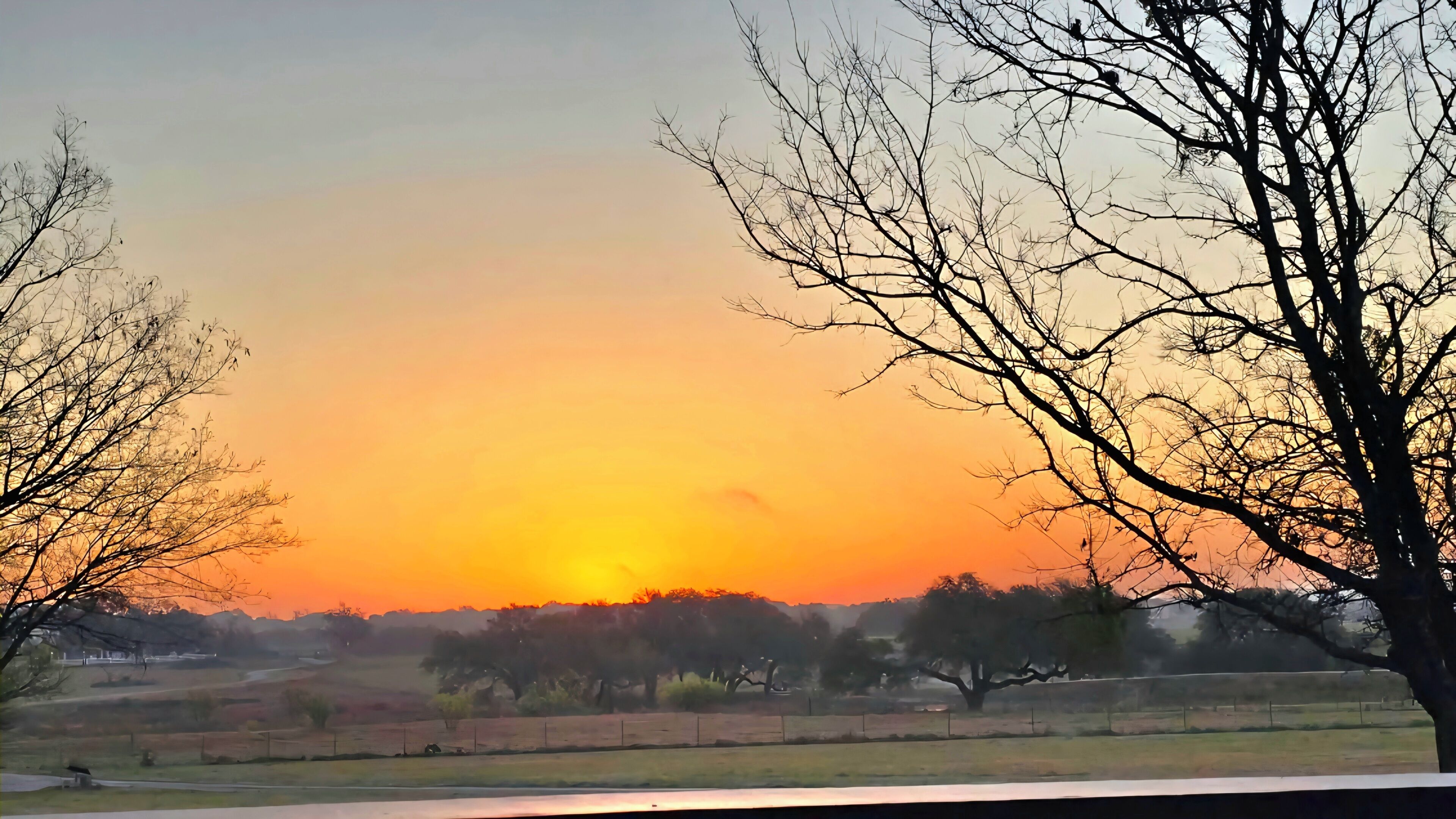 A sunset over a rural landscape with trees and open fields.