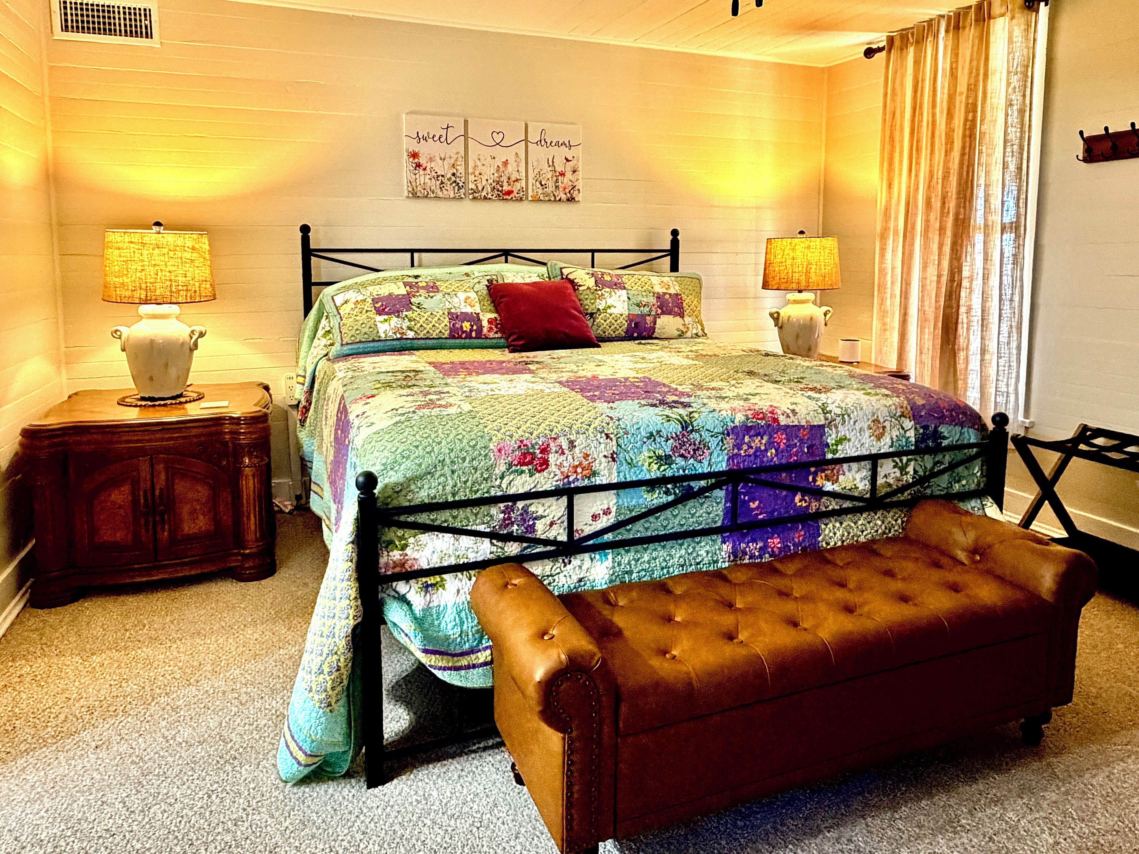 Ein Schlafzimmer mit einem Bett, zwei Nachttischen, einer Bank und einer Wand mit Blumenbild.