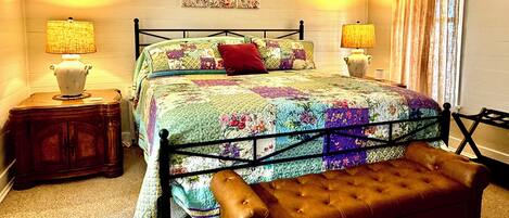 Ein Schlafzimmer mit einem Bett, zwei Nachttischen, einer Bank und einer Wand mit Blumenbild.