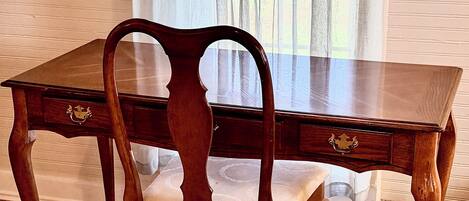 Una mesa de madera para comer con dos sillas, una ventana con cortinas ligeras y un suelo alfombrado.