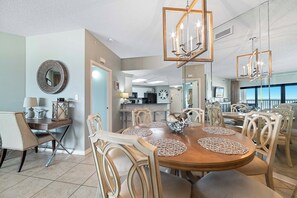 A dining area with a wooden table, chairs, and a chandelier. - The Palms West 515 | Beachfront | Pools | My Beach Getaways (Orange Beach)