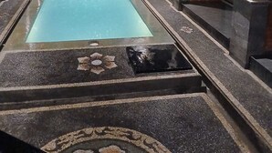 A swimming pool with a tiled deck, surrounded by covered seating areas with pillars and a brick wall. - Ulu Bali Homestay (Jimbaran)