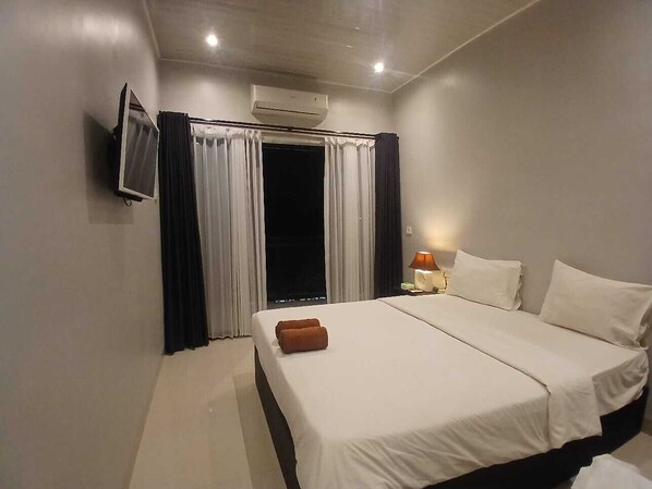 Habitación de hotel con cama, televisor montado en la pared, ventana con cortinas y aire acondicionado.