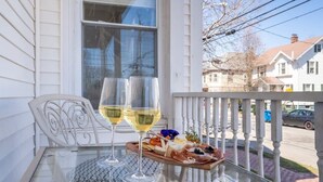 Una mesa de cristal con dos copas de vino y una tabla de embutidos en un balcón.