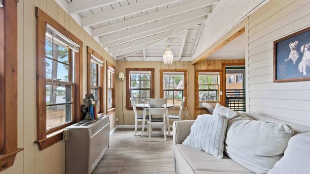 A cozy room with a wooden ceiling, a dining table with chairs, a sofa, and a radiator. - Long Lake Cabin: Shared Beach, Grill, Porch (Naples)
