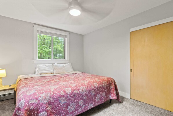 A bedroom with a bed, a window, a ceiling fan, and a wooden door.