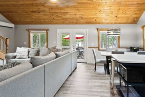 A modern living room with a grey sectional sofa, a dining table with chairs, and a kitchen area with a white countertop and appliances. - Spacious Family Home w/ Long Lake Access (Naples)