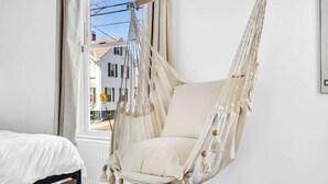 Une pièce avec un lit, un fauteuil suspendu et une fenêtre donnant sur des immeubles.