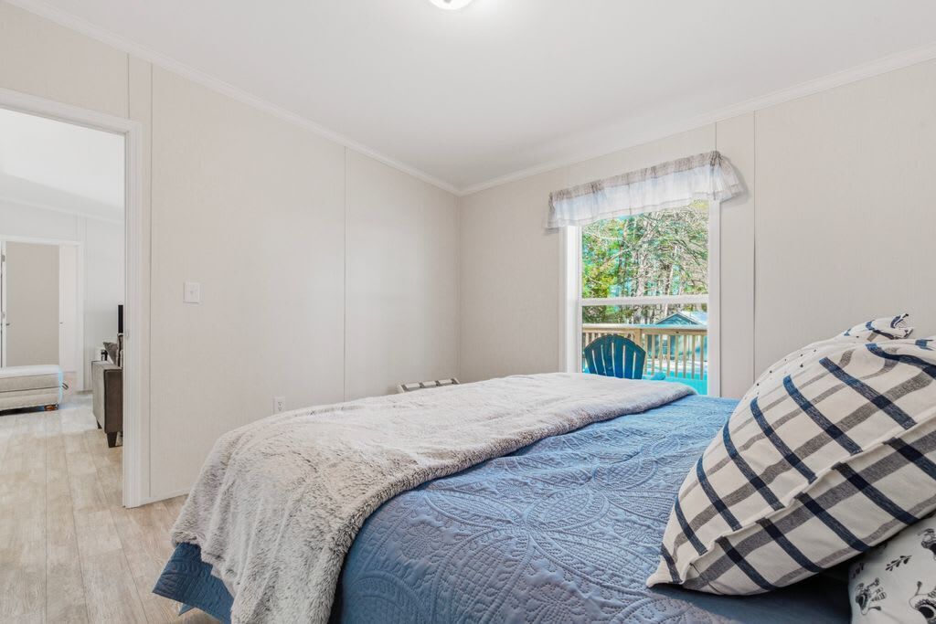Une chambre à coucher avec un lit, une fenêtre donnant sur un espace verdoyant et une porte menant à une autre pièce.
