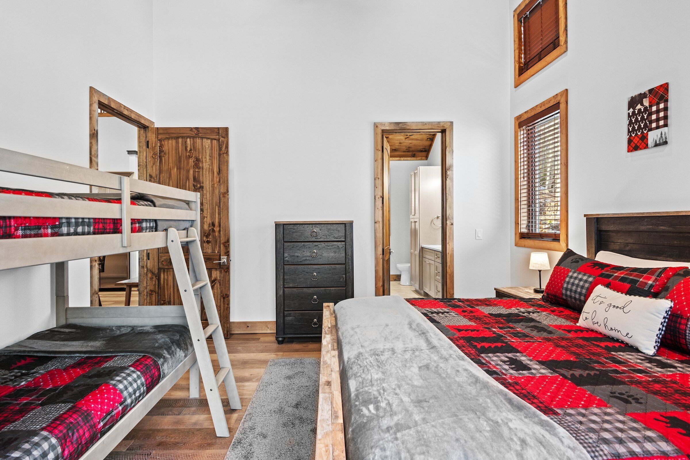 A bedroom with bunk beds, a dresser, a mirror, and a bed with a patterned blanket.