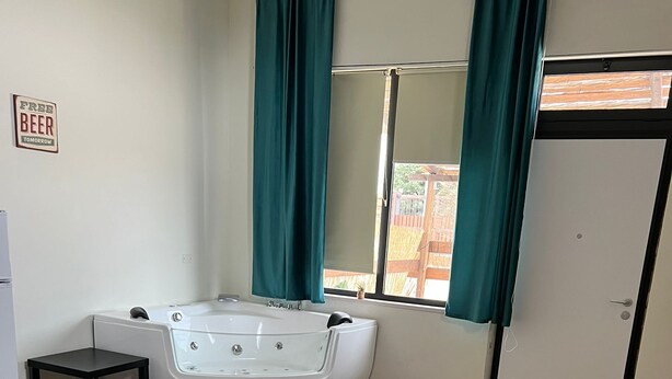 A modern room with a wooden floor, a round table with a plant, a black rug, a white chair, a teal sofa, a bathtub, and a door with a sign. - Villa Uma with Private Jacuzzi and Secure Parking - 5 Minutes from the Sea (Puglia)