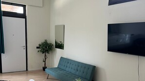 A modern living room with a teal sofa, two white chairs, a round wooden coffee table with a plant, a flat-screen TV mounted on the wall, and a door with a green curtain. - Villa Uma with Private Jacuzzi and Secure Parking - 5 Minutes from the Sea (Puglia)