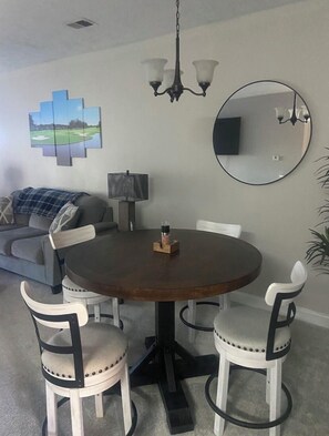 Ein Essbereich mit einem runden Tisch, vier Stühlen, einer Chandelierleuchtre, einem runden Spiegel und einem Gemälde an der Wand.