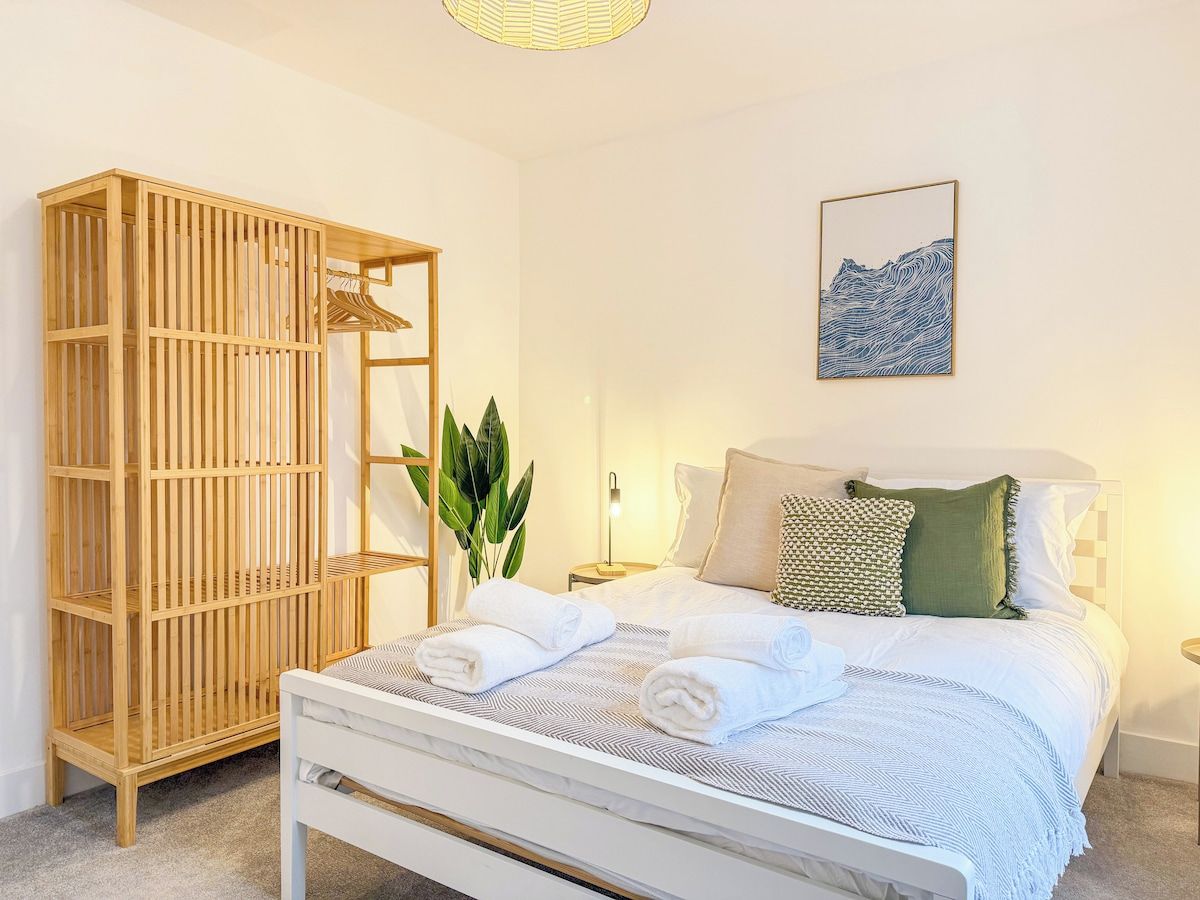 Un dormitorio con cama, armario de madera, mesita de noche con lámpara y una obra de arte colgada en la pared.