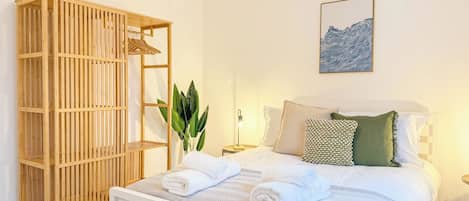 A bedroom with a bed, a wooden wardrobe, a bedside table with a lamp, and a wall-mounted artwork.