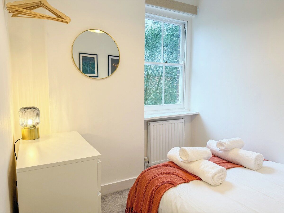 Une chambre à coucher avec un lit, une table de chevet, une lampe, un miroir et une fenêtre.