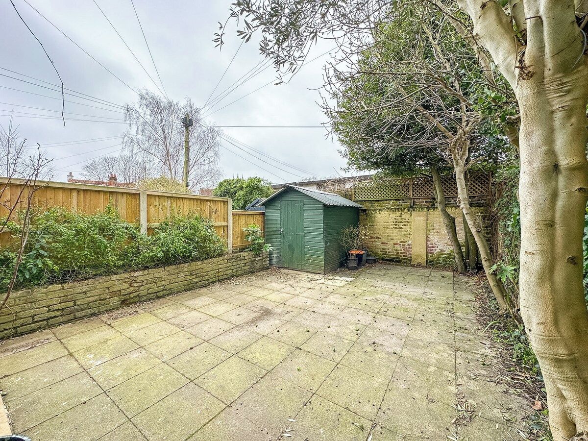 Un jardin avec un abri de jardin vert, un mur de briques et une clôture en bois.