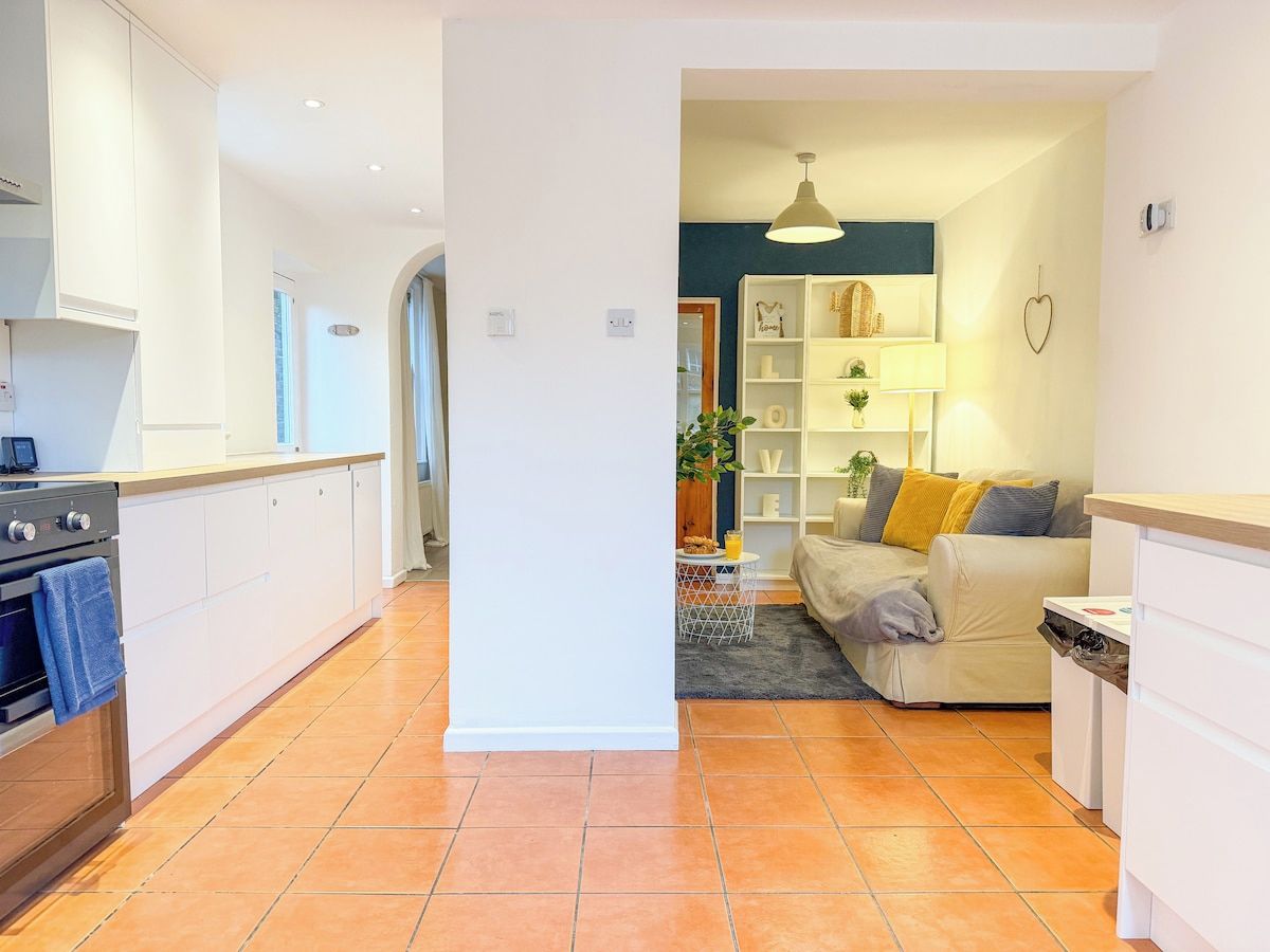A modern kitchen with white cabinets, a stove, and a dining area with a sofa and a lamp.