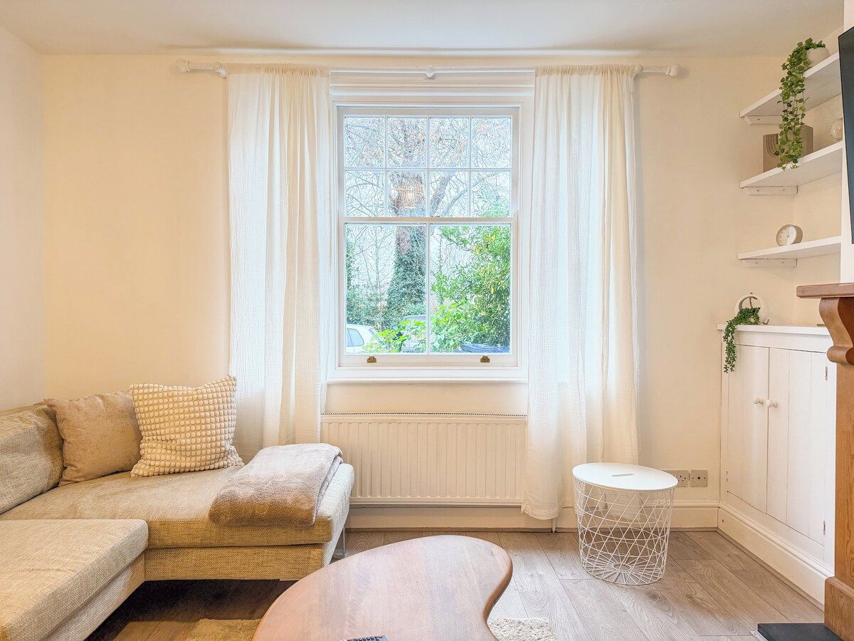 Un salon confortable avec un canapé, une petite table, un radiateur et une fenêtre avec des rideaux.