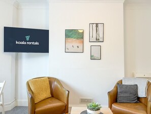 Een zithoek met twee leren fauteuils, een flatscreen televisie en kunstwerken in lijsten aan de muur.