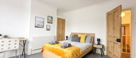 A bedroom with a bed, bedside tables, a desk, and a radiator.