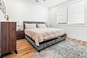 A bedroom with a bed, wooden dresser, bedside lamps, and a patterned rug.