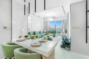 Ein modernes Hotelzimmer mit Essbereich, einem grünen Sofa und Blick auf die Stadt.