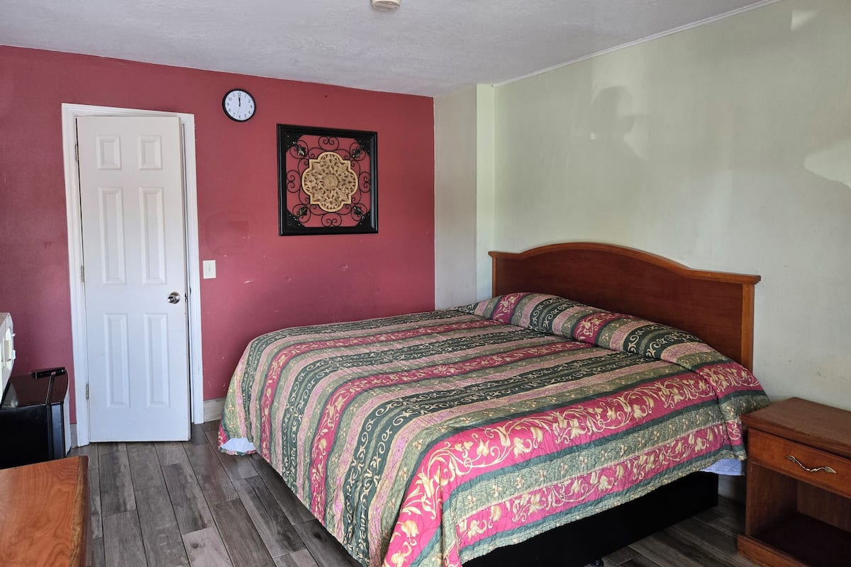 Un dormitorio con una cama de madera, una puerta blanca, un reloj de pared y un adorno enmarcado.