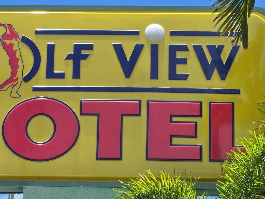 A yellow sign with 'GOLF VIEW MOTEL' in bold letters, a golf ball, and a golfer silhouette.