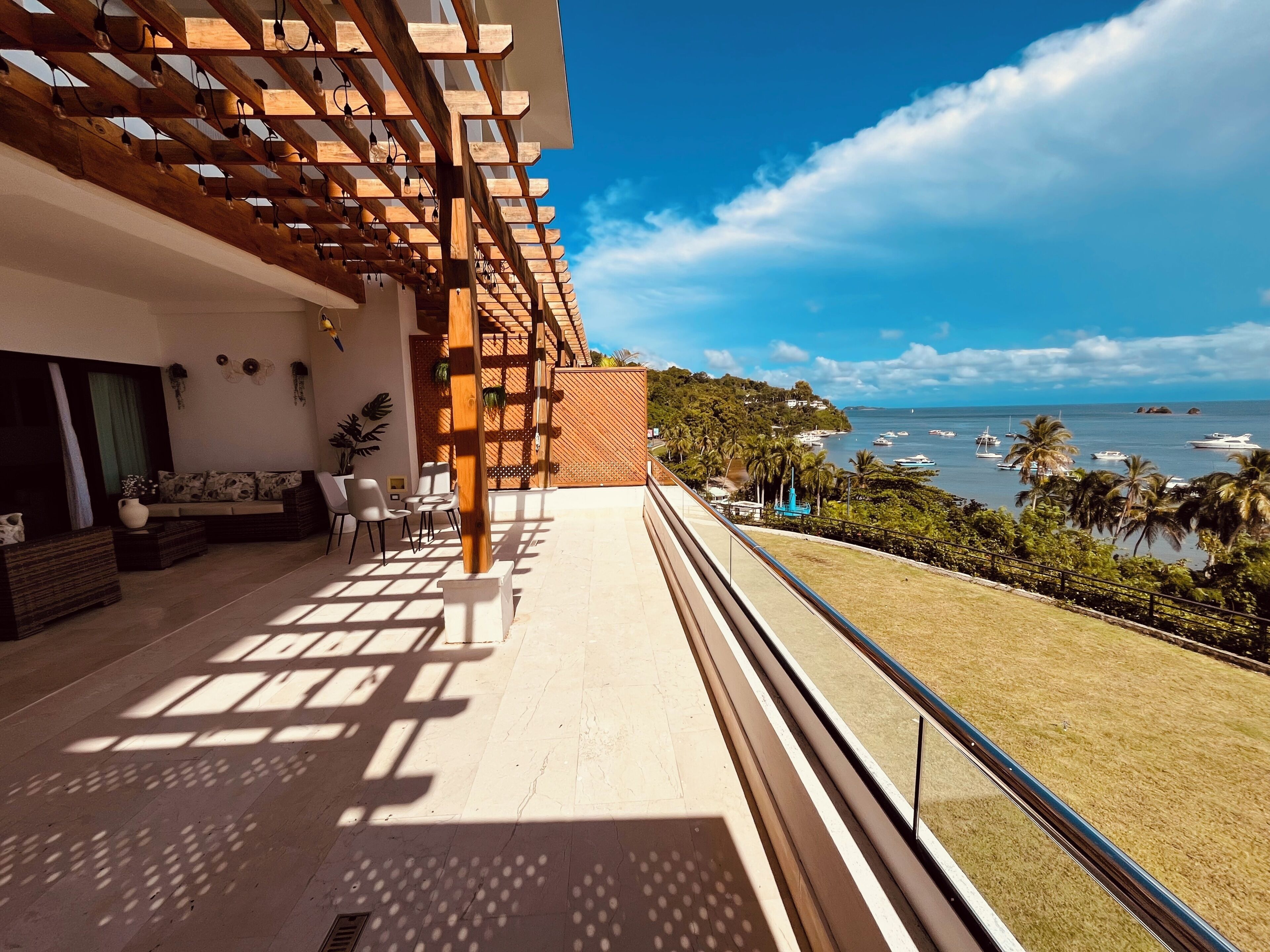 Un balcone con vista sul mare, una pergola in legno e un'area salotto all'aperto.