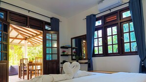 Une chambre d’hôtel avec un lit, un bureau et une chaise. Il y a une fenêtre avec des rideaux et une vue sur la verdure à l’extérieur.