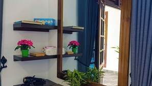 Une salle de bain avec une étagère en bois sur laquelle sont posés un sèche-cheveux, un miroir et une plante en pot.