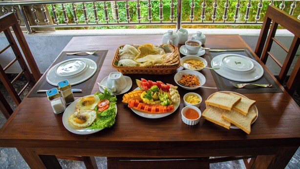 Une table à manger dressée avec divers plats, notamment des œufs, une salade et du pain, sur un balcon offrant une vue sur une végétation luxuriante.