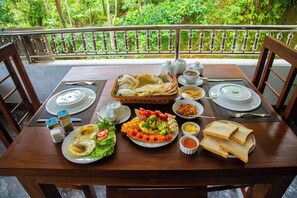 A dining table set with various dishes, including eggs, salad, and bread, on a balcony with a view of lush greenery. - Bridge Front Inn Ella (Ella)