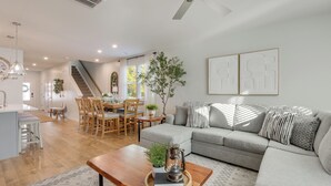 A modern living room with a grey sofa, wooden coffee table, and a dining area with wooden chairs and a table.