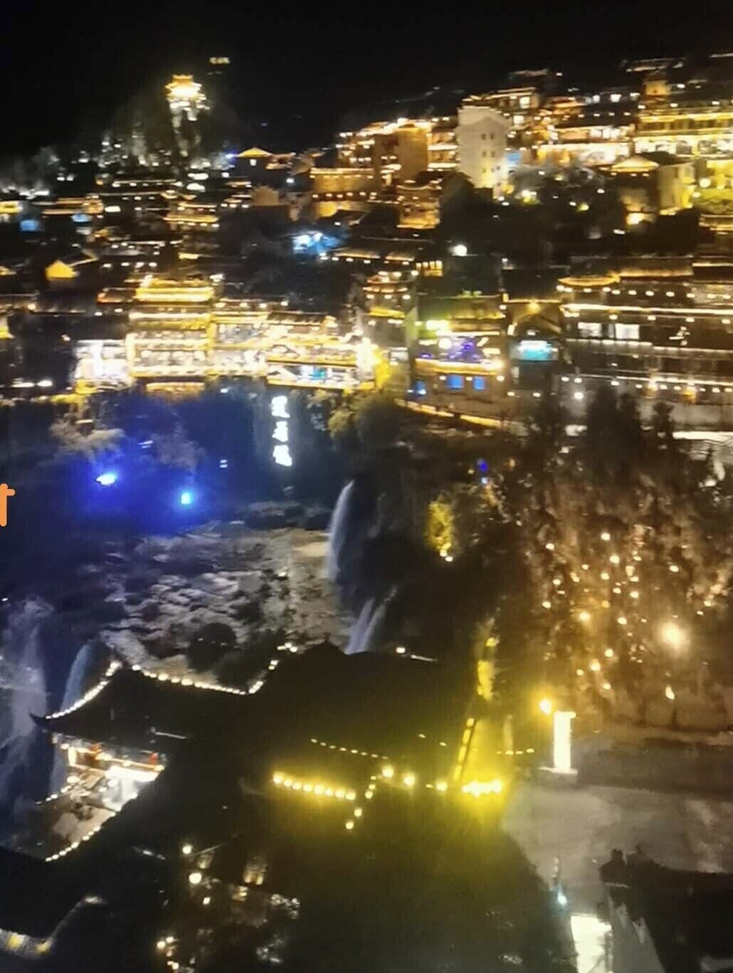 A nighttime view of a historic town with illuminated buildings and a river.