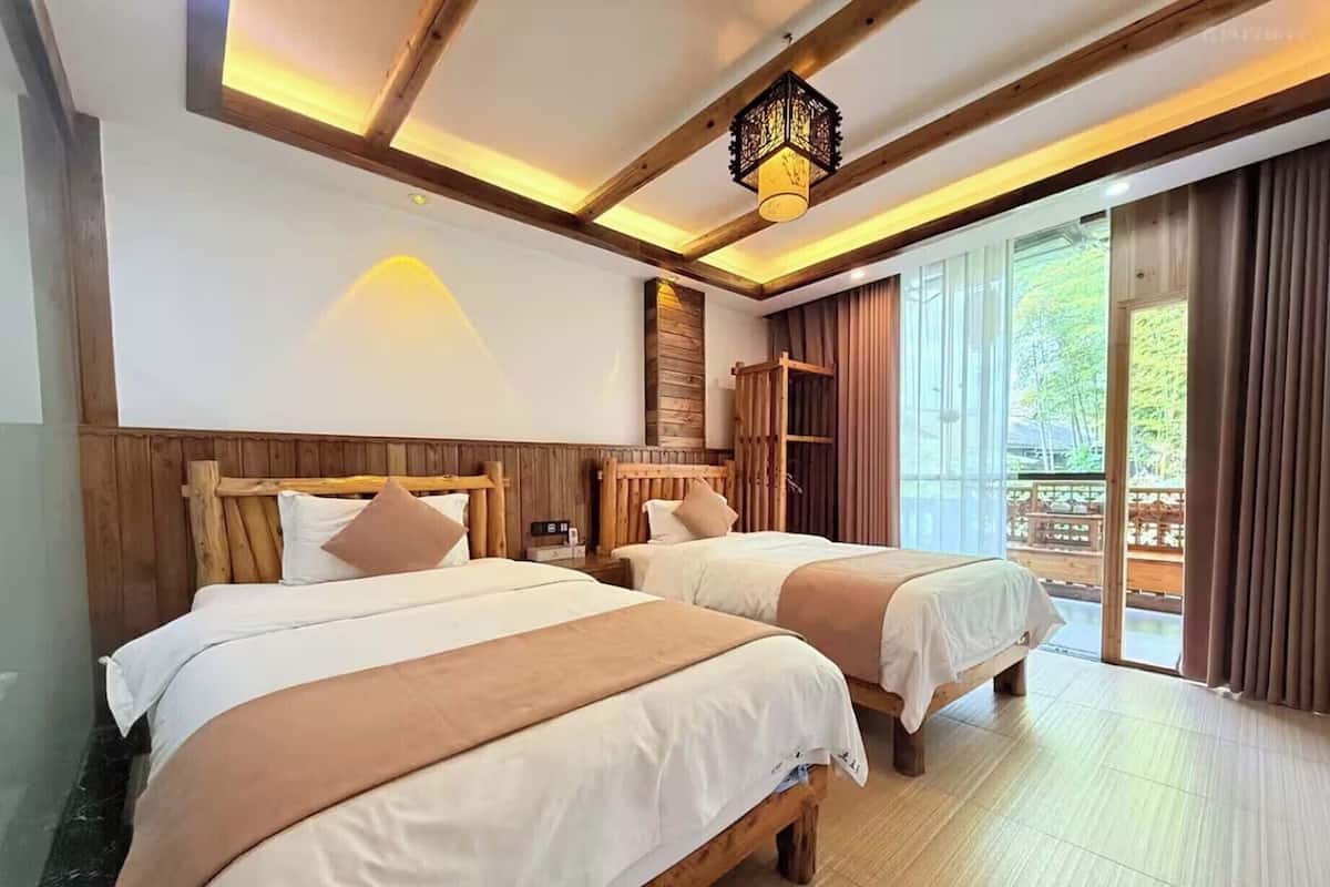 Ein Hotelzimmer mit zwei Betten, Holz-Kopfteilen, einem großen Fenster mit Vorhängen und einer Holzbalkendecke.