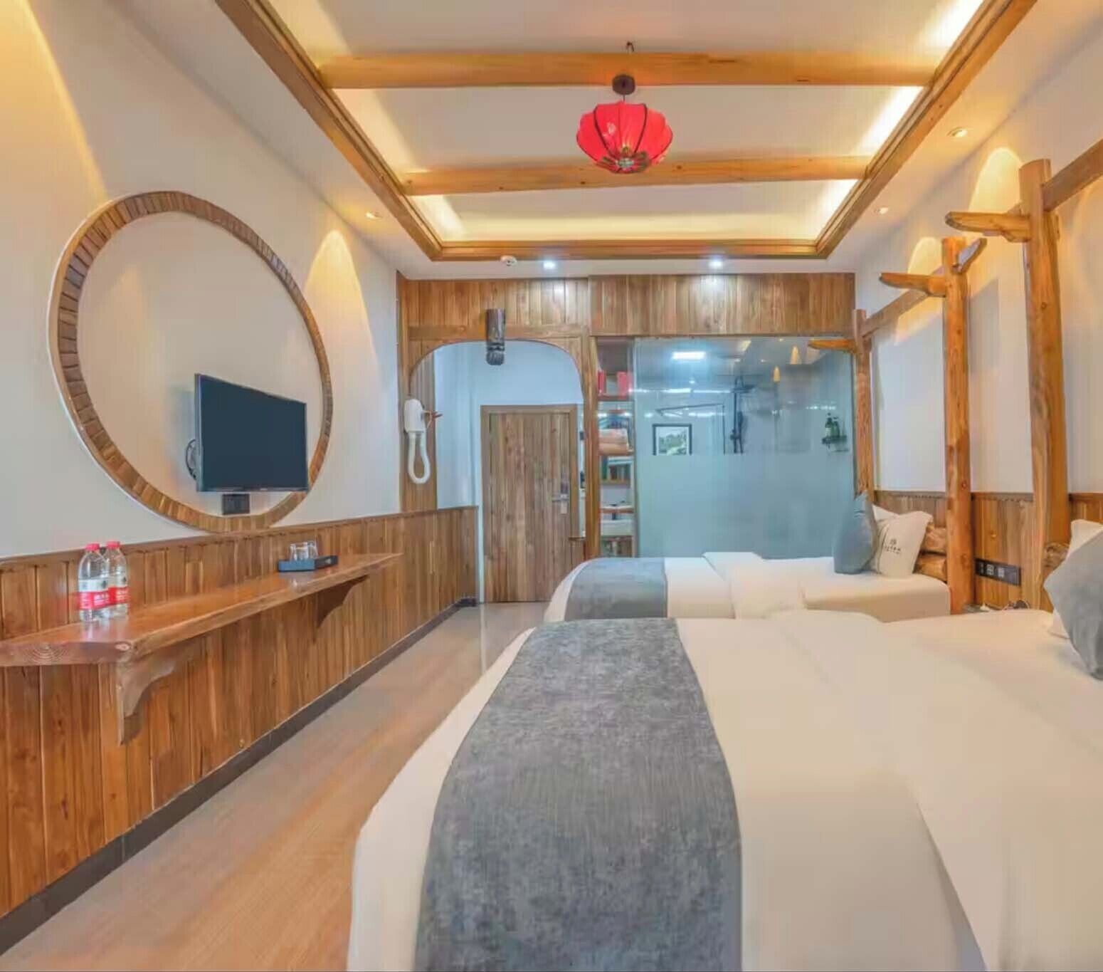 A hotel room with a large bed, a round mirror, a wooden reception desk, and a red hanging light fixture.