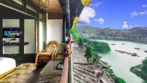 Een balkon met uitzicht op een rivier en traditionele gebouwen, een televisie, rieten meubels en een hanglamp.