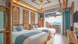 Een hotelkamer met twee bedden, houten meubels, een balkon met uitzicht en een televisie aan de rechterkant.