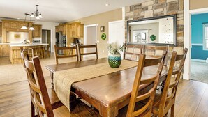 A spacious dining area with a wooden table and chairs, a kitchen in the background, and a stone accent wall. - Family Home on 9 Acres! Climbing Wall & Gym (Thornville)