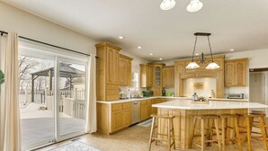 A spacious kitchen with wooden cabinets, a large island with bar stools, and a sliding glass door leading to a patio. - Family Home on 9 Acres! Climbing Wall & Gym (Thornville)