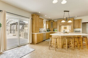 Eine geräumige Küche mit Holzausbau, einer großen Kochinsel mit Barhocker und einer Glastür zum Patio.