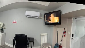 Quarto de hotel compacto com cozinha compacta, cama com cabeceira, televisão e pequena mesa de cabeceira.